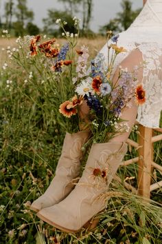 a woman sitting on a chair with flowers in her boots and holding the leg of another person's boot