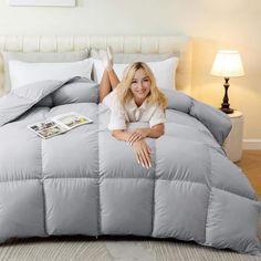 a woman laying on top of a bed covered in grey comforter and pillow covers