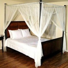 a four poster bed with white sheets and pillows on top of wooden flooring in a bedroom