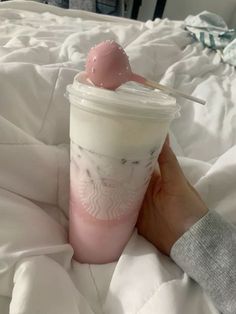 a person holding a starbucks cup with a cherry in it on top of a bed