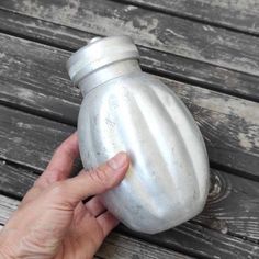 a hand is holding a metal container on a wooden surface