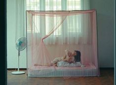 a woman laying on top of a bed next to a baby in a pink net