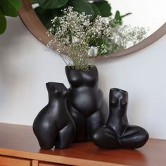 three black vases sitting on top of a wooden table next to a mirror and plant