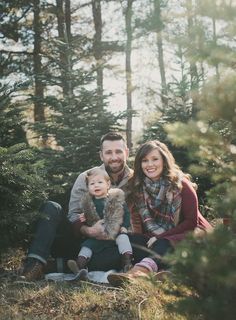 a man and woman are sitting in the woods with their baby boy, who is wearing a fur hat