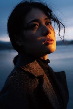 a woman standing in front of the ocean at night with her hair blowing in the wind