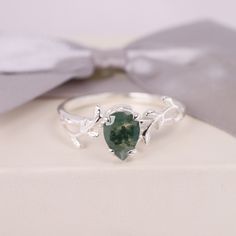 a close up of a ring with a green stone on the front and silver leaves on the back