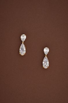 two pear shaped diamond earrings on a brown background, one is white and the other is yellow