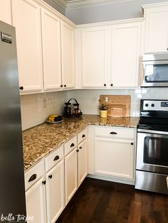 a kitchen with white cabinets and granite counter tops, stainless steel appliances and wood flooring