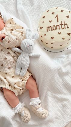 a baby is sleeping next to a 1 month old cake and stuffed animal on a bed