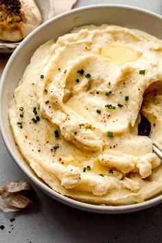 a bowl filled with mashed potatoes topped with butter and seasoning next to garlic