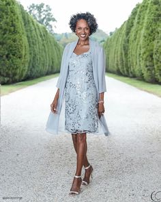 a woman in a blue dress and jacket walking down a path with trees behind her