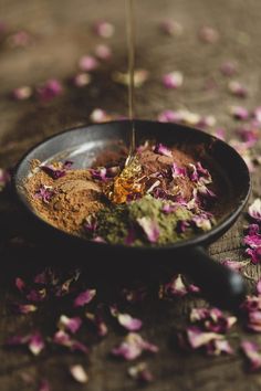 a bowl filled with dirt and flowers on top of a wooden table covered in petals