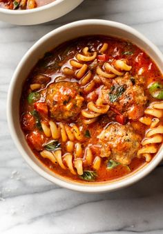 two bowls filled with pasta and meatballs on top of a white table next to another bowl