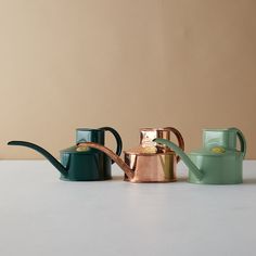 three pots and a watering can sitting on a table