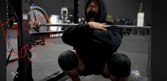 a man squats on the ground in front of a barbell with his hands behind his back