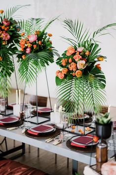 the table is set with orange and pink flowers in vases on top of black plates