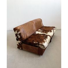 a brown and white cow print couch with pillows on it's back, sitting against a wall