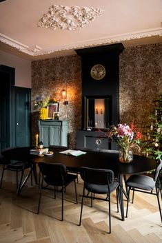 a dining room table with black chairs and a clock on the wall above it, in front of a fireplace