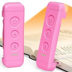 two pink video game controllers sitting next to an open book