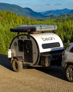 an off road camper parked on the side of a dirt road with mountains in the background