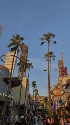 people are walking down the street in front of palm trees