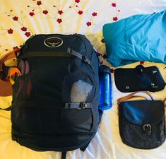 an open backpack sitting on top of a bed next to other bags and purses