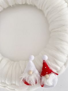 a white wreath with two gnomes on it and a red santa hat hanging from the front