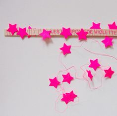 some pink stars are hanging on a white wall and there is a sign that says des moltettes