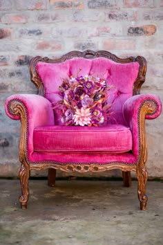 a pink chair with flowers on it in front of a brick wall