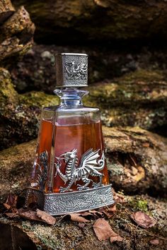 a glass bottle with a silver dragon on it sitting on the ground next to rocks