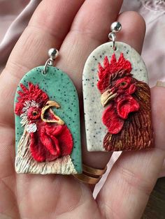 two handmade earrings with roosters on them, one is green and the other is red