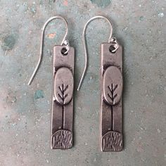 pair of earrings with tree design on them sitting on concrete surface next to cement wall