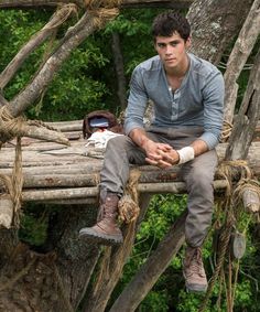 a man sitting on top of a wooden bench in the middle of a tree filled forest