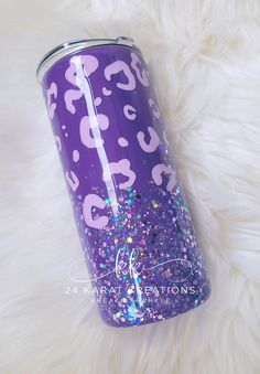 purple and pink glitter tumbler sitting on top of a white fur covered floor next to a metal can