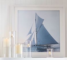 a white shelf topped with candles next to a framed sailboat photo on the wall