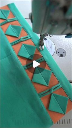 the sewing machine is working on an orange and green piece of paper that has been cut into triangles