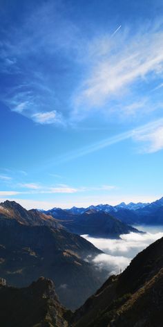 the mountains are covered in low lying clouds and blue skies with white wispy clouds