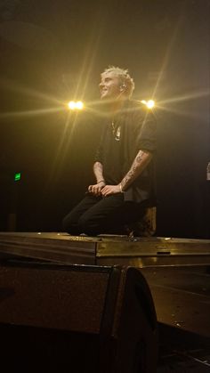 a man sitting on top of a wooden table in front of a spotlight filled stage