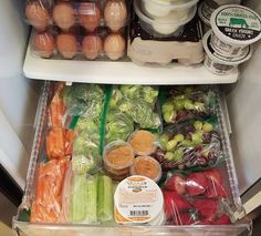 an open refrigerator filled with lots of fresh vegetables and eggs in plastic containers on the shelves