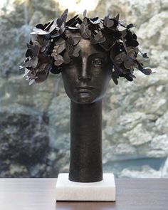 a statue head with leaves on it sitting on a table next to a rock wall