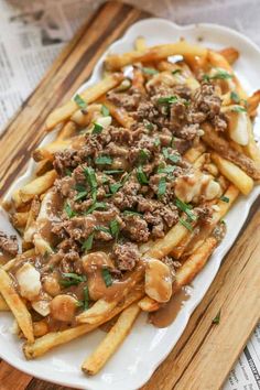 french fries with meat and gravy on a white plate next to a wooden cutting board