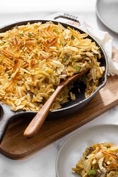 a skillet filled with pasta and vegetables on top of a wooden cutting board next to plates