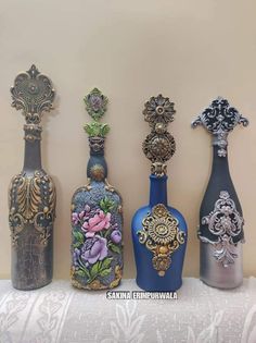 four vases are lined up on a table with white lace and wallpaper in the background