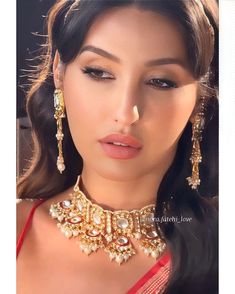 a woman in a red dress with gold jewelry on her neck and nosepieces