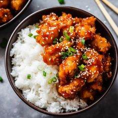 two bowls filled with chicken and rice next to chopsticks on a table top