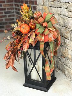 a lantern decorated with fall leaves and pumpkins is sitting on the ground next to a brick wall