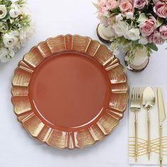 an orange plate with gold rim sits on a table next to silverware and flowers