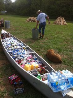 a canoe filled with water bottles and other items sitting on the grass in front of a man