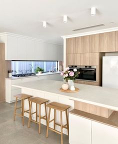 a kitchen with white counter tops and wooden stools next to an island in the middle