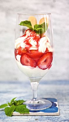 a dessert in a wine glass with strawberries and whipped cream on the rim, garnished with mint leaves